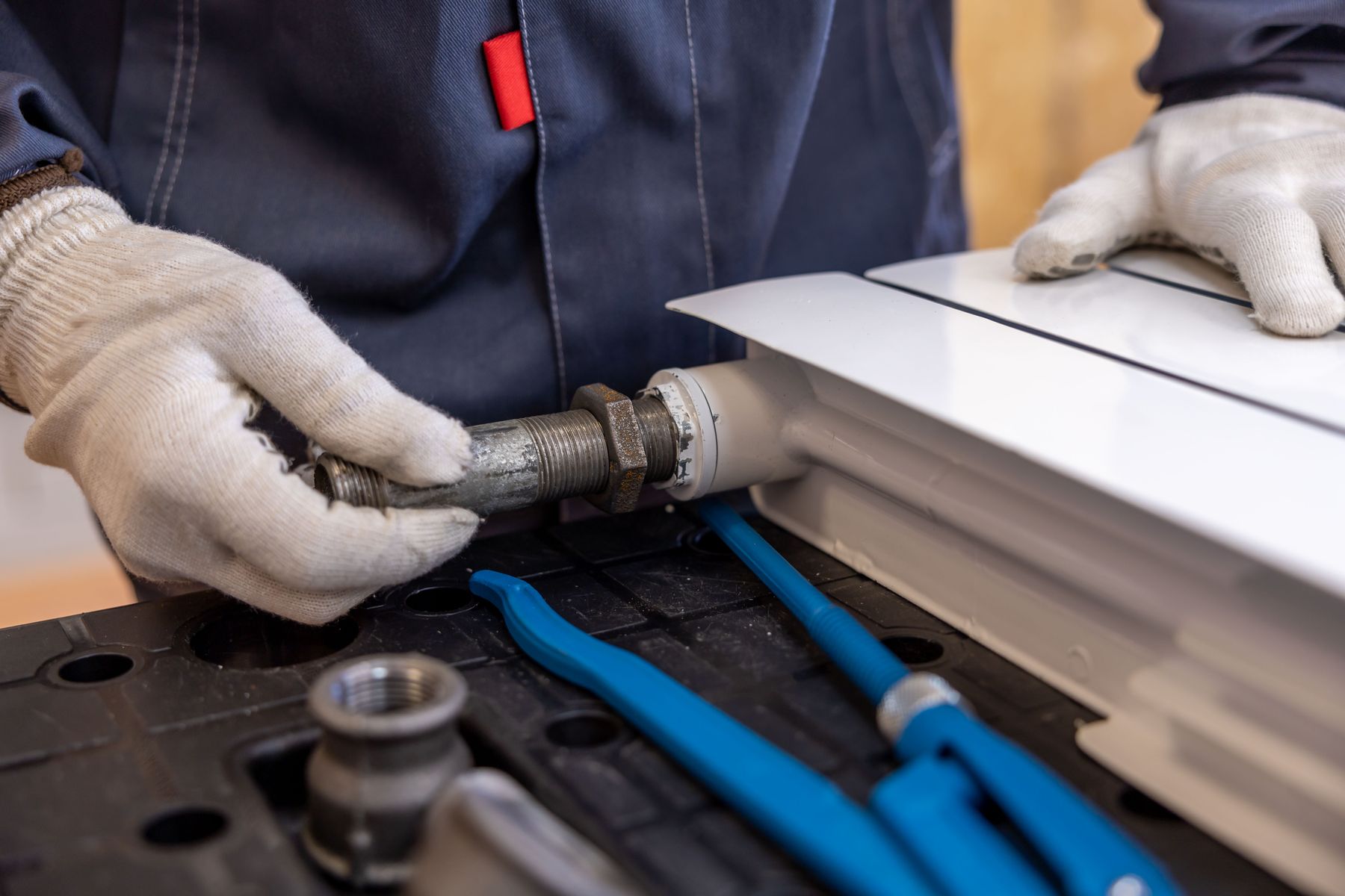Gloved hands fitting a valve tail to a white radiator on a workbench